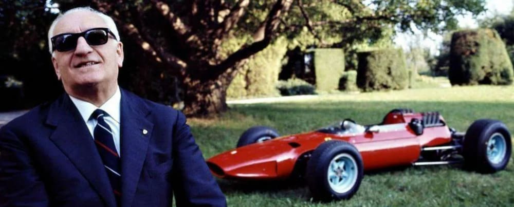 Enzo Ferrari con un Ferrari de competición al fondo